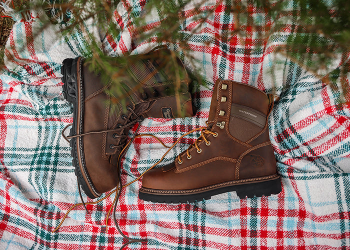 Pair of brown boots on a red, green, and white plaid fabric with Christmas tree branches.