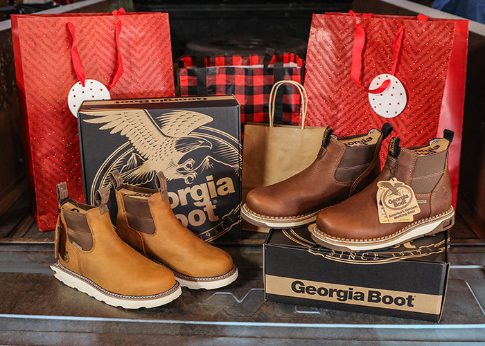 Pair of brown boots on a Georgia Boot box with red gift bags in the background.